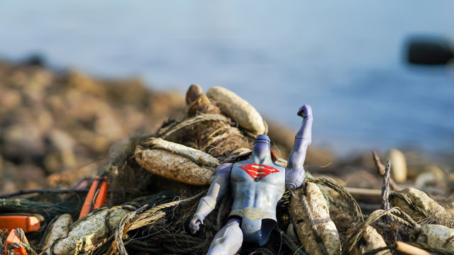 En ødelagt superhelt-leke ligger blant tau og søppel ved vannkanten.