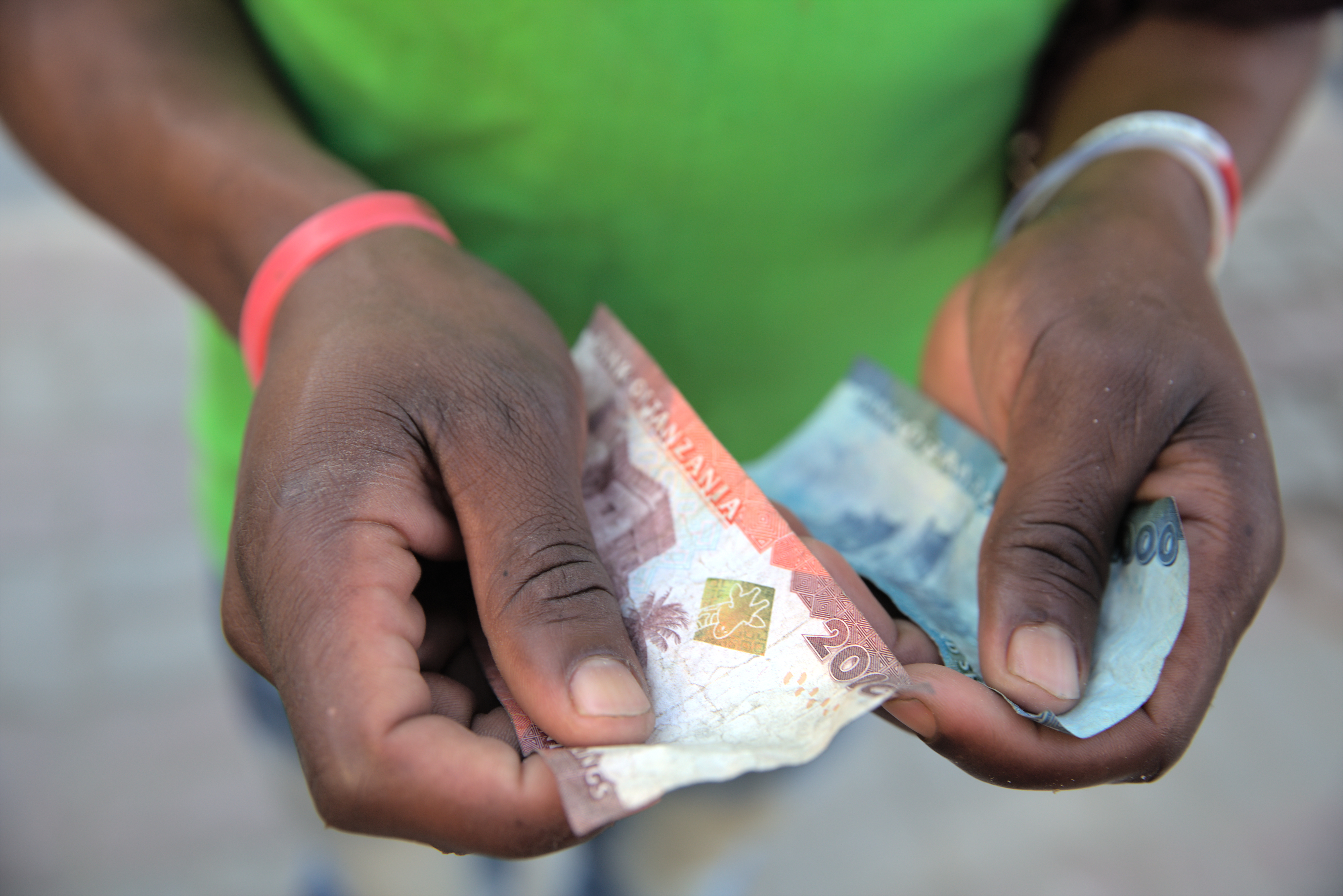 En person holder tanzanianske sedler i hendene, med fokus på pengene.