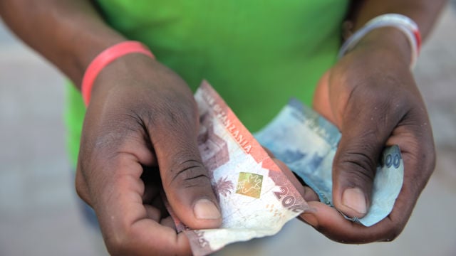 En person holder tanzanianske sedler i hendene, med fokus på pengene.