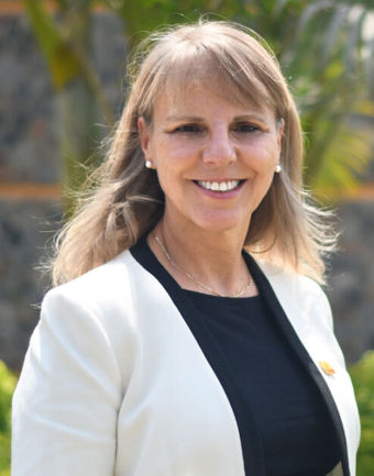 Portait of Dr. Sandra Cristina Kothe Milach. She is standing in a white blazer and black sweater, in front of a garden background. 