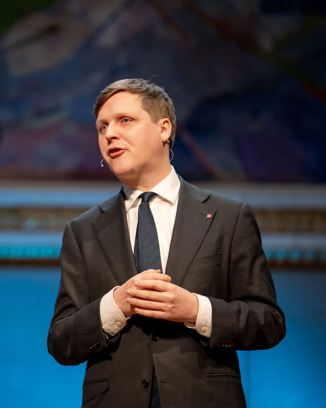 En ung mann i dress står på en scene. 