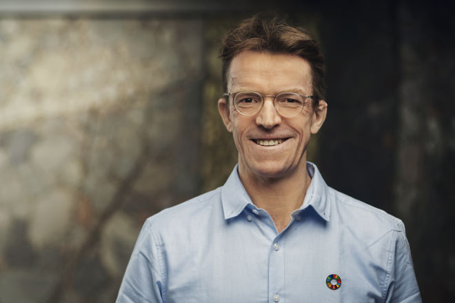 En mann med blå skjorte står foran en uklar bakgrunn.