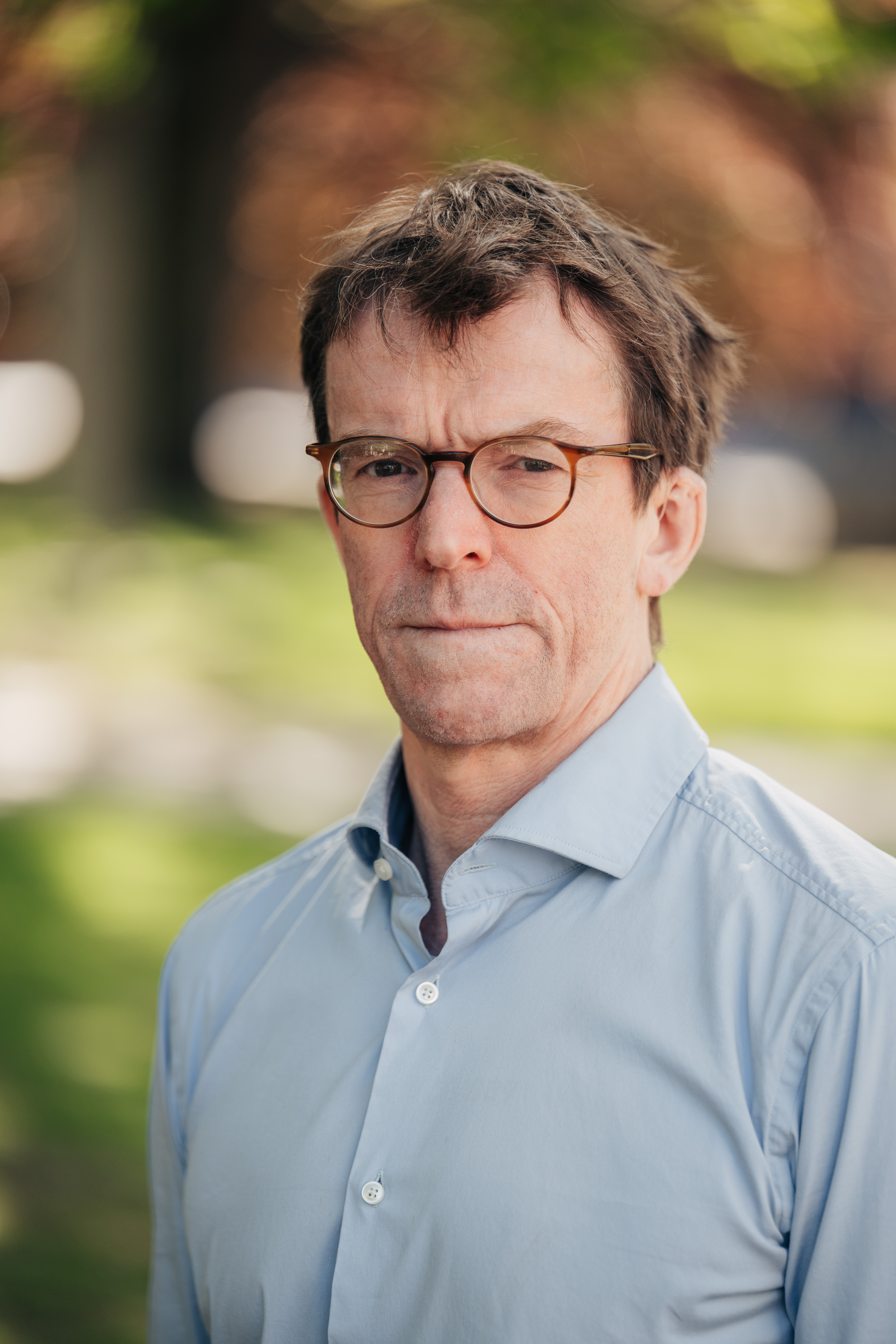 Ett protrett av nn voksen mann i lyseblå skorte står utendørs og ser i kamera.