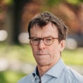 Ett protrett av nn voksen mann i lyseblå skorte står utendørs og ser i kamera.