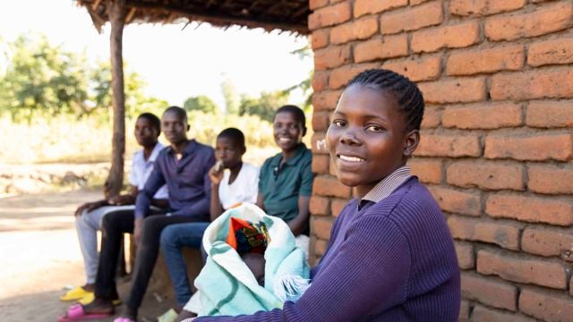 Young African woman holding a baby smiles at the camera.