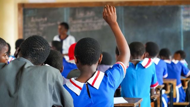 Classroom with students in blue uniforms. One girl is raising her hand.