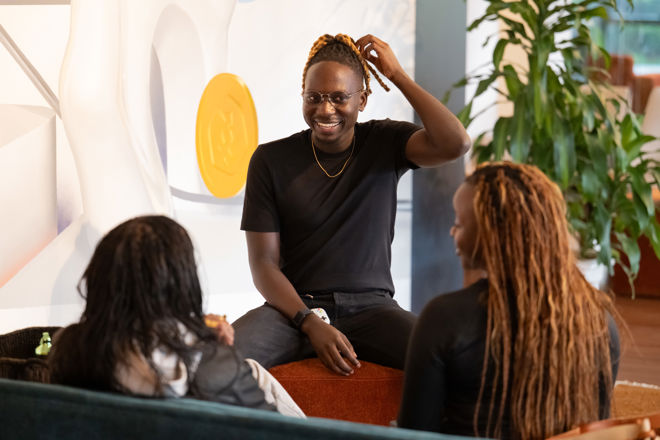 Tre unge personer sitter og prater sammen innendørs i et loungeområde.