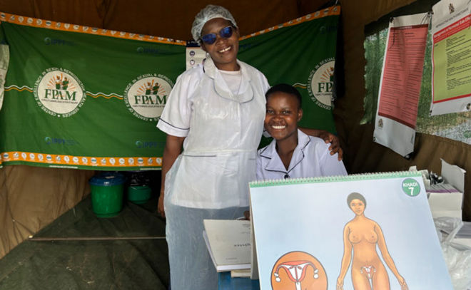 To helsearbeidere i hvite uniformer står i et telt med informasjonsmateriell om seksuell og reproduktiv helse.