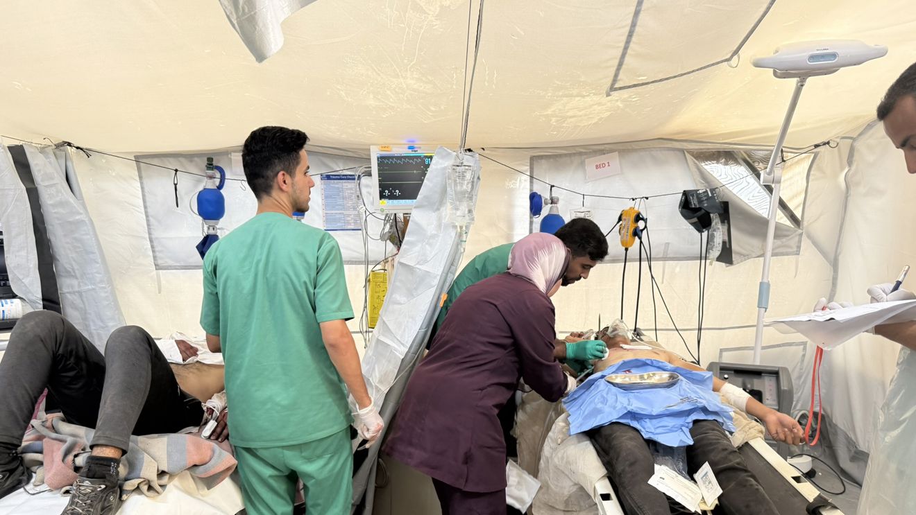 Medical personnel in scrubs treat patients lying on beds inside a temporary medical tent.