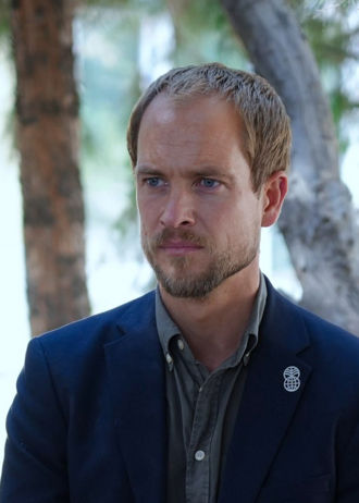 Portrett av Erik Abild. Han står med kort lyst hår iført skjorte og mørk jakke med Norad-logo på en nål, utendørs foran trær.