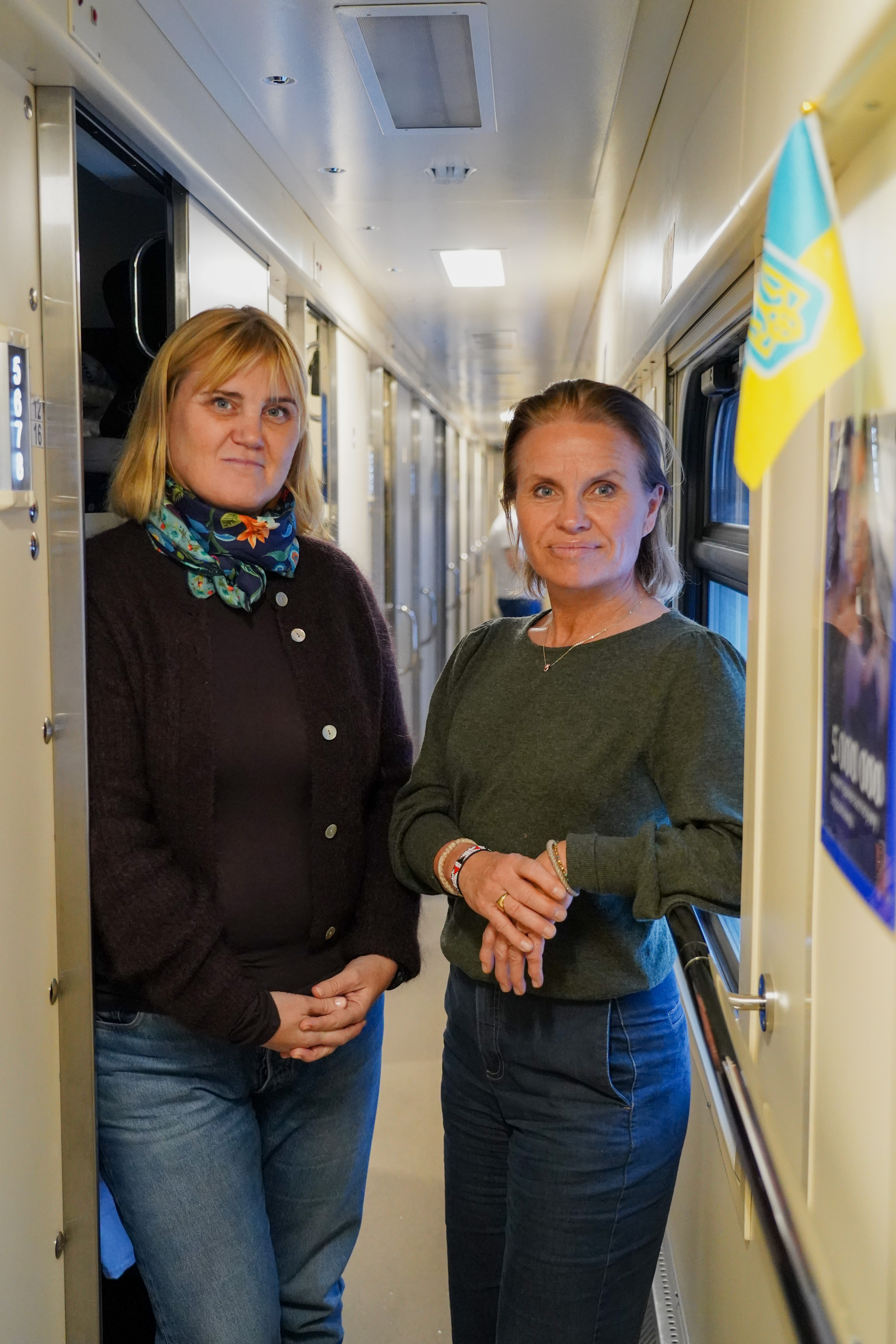 To kvinner står i en smal togvogn og ser i kameraet. 