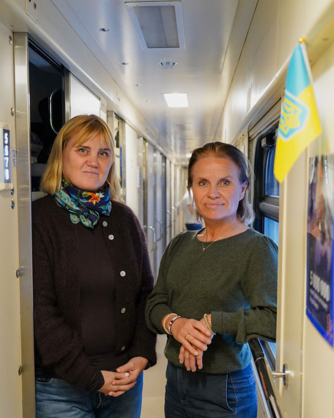 To kvinner står i en smal togvogn og ser i kameraet.