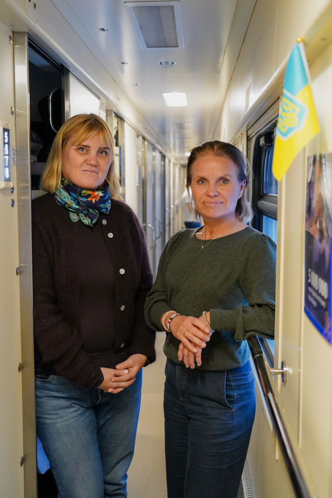 To kvinner står og snakker sammen i en smal korridor på et tog, med et ukrainsk flagg i forgrunnen.