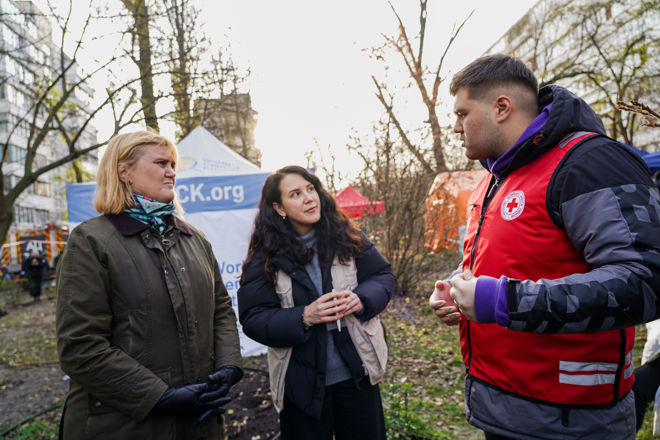 To kvinner og en mann fra Røde Kors står og samtaler utendørs foran et telt.