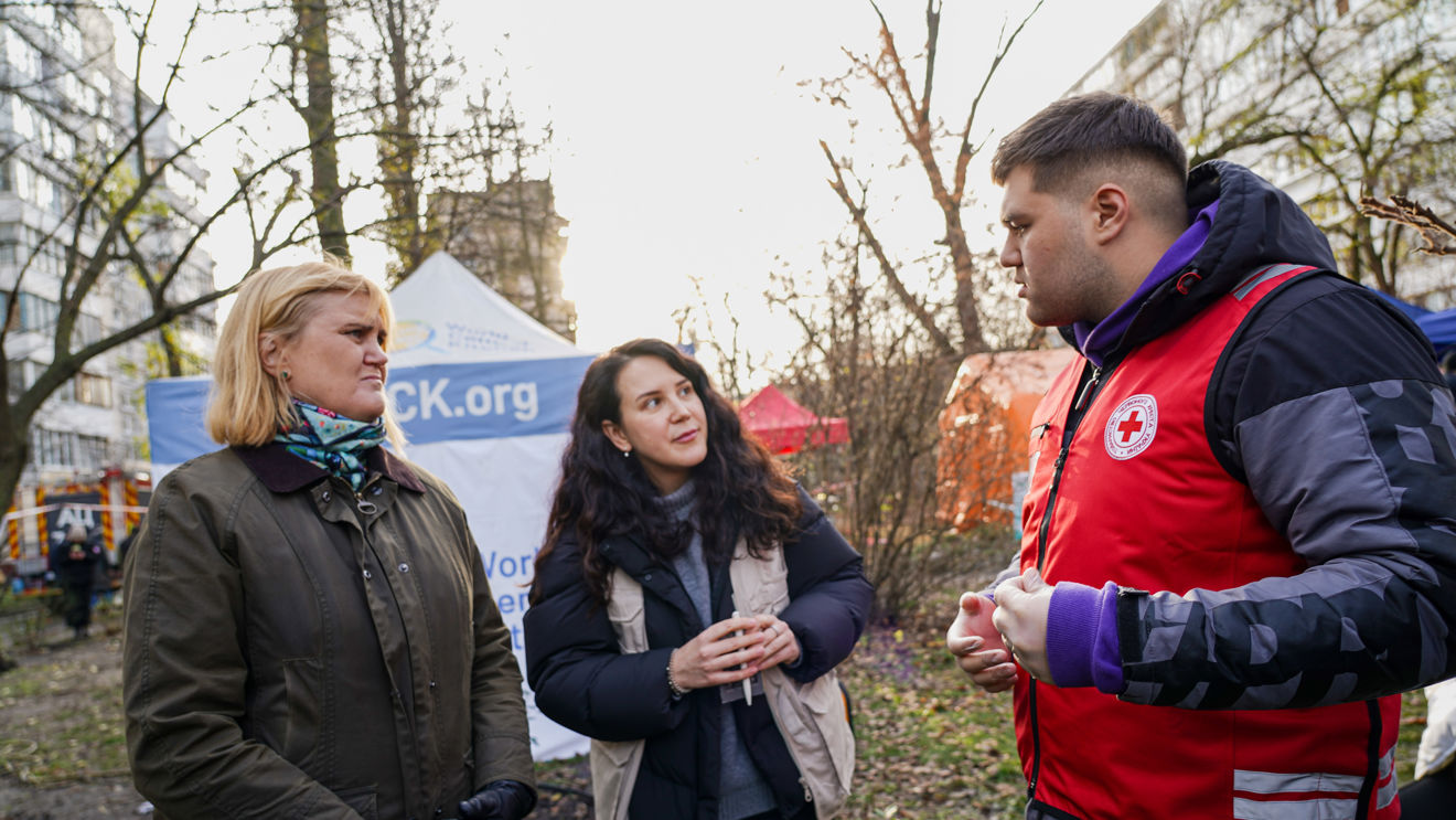 To kvinner og en mann fra Røde Kors står og samtaler utendørs foran et telt.