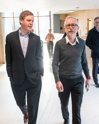 To menn i dress og formelle klær går ved siden av hverandre inne.