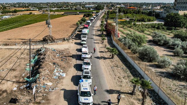 White UN vehicles are driving in a column on a road.