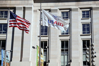 Det amerikanske flagget og flakket til USAID foran hvit byning. 