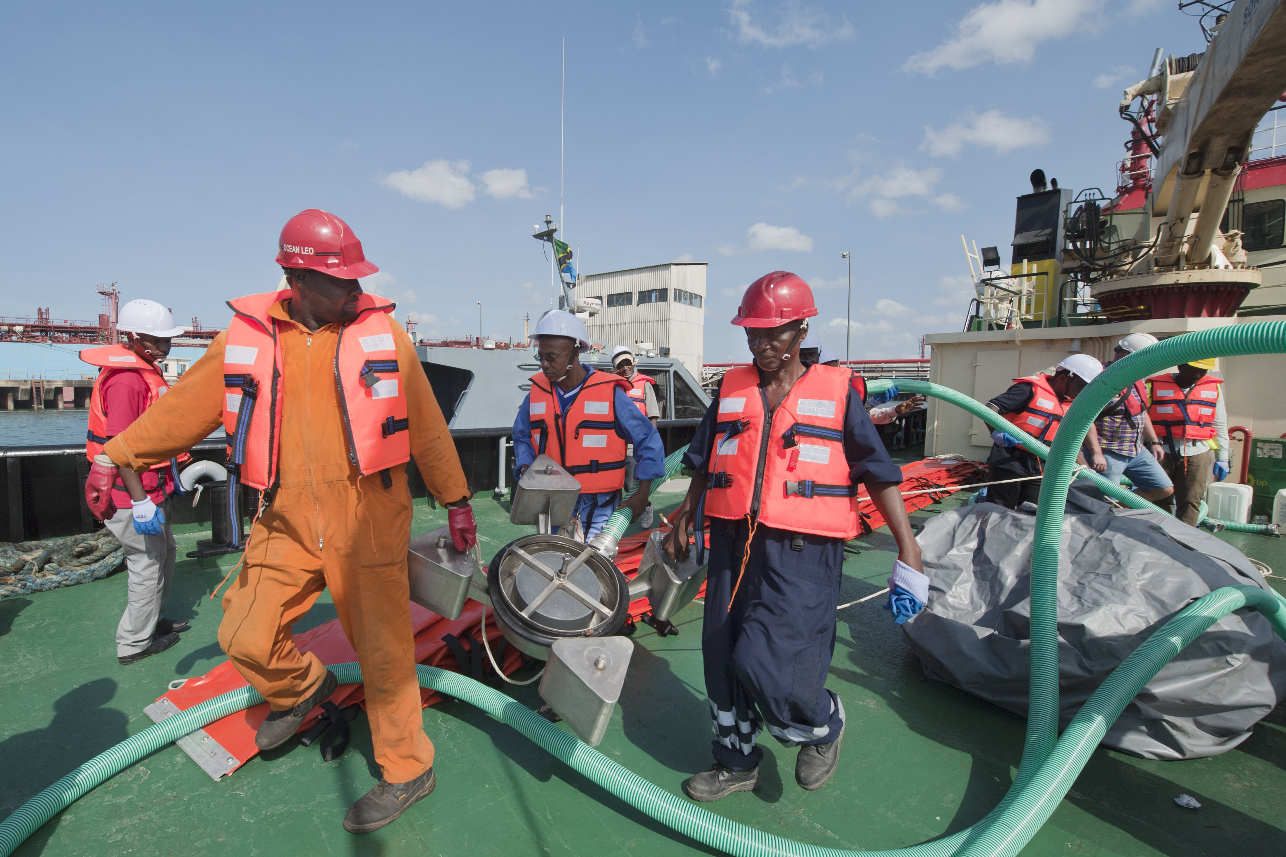Fem menn i Orange vester og hjelp står på dekket på en grønn båt. 