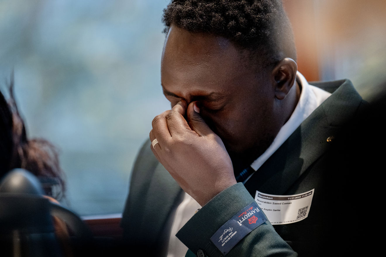 Bildet viser en mann fra Sudan, kledd i en mørk dressjakke og hvit skjorte. Han sitter innendørs og holder hånden opp til ansiktet.
