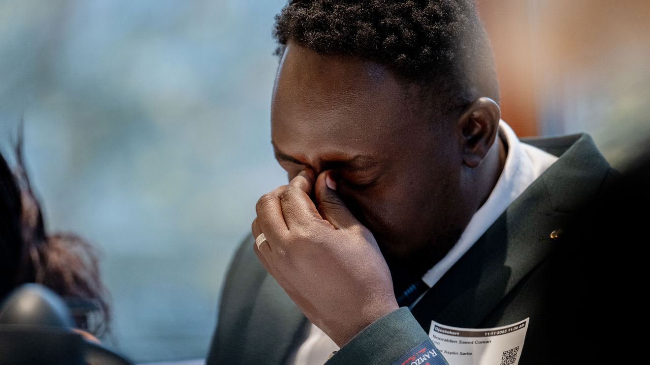 Bildet viser en mann fra Sudan, kledd i en mørk dressjakke og hvit skjorte. Han sitter innendørs og holder hånden opp til ansiktet.