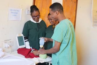 Three doctors are standing over a baby smiling. 
