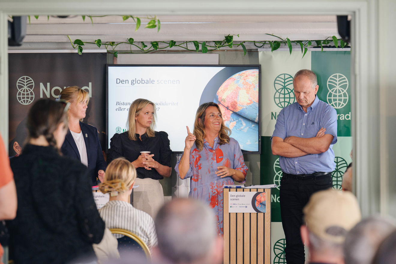 Fire voksne personer står foran et publikum under et Norad-arrangement. Kvinnen i midten snakker og holder en finger opp, mens de andre står ved siden av og lytter.