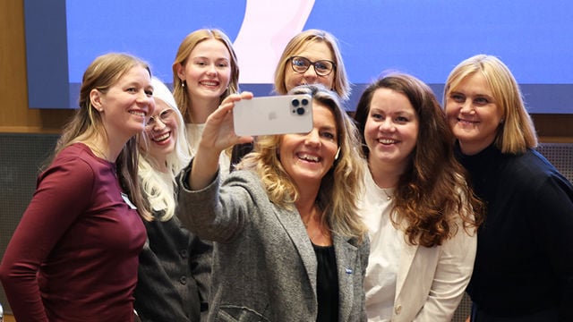 En gruppe kvinner smiler og samler seg foran en mobiltelefon som kvinnen i forgrunnen holder opp for å ta en selfie.