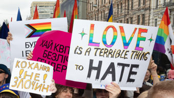 Ei folkemengd deltek i ei pride-markering og held opp plakatar med bodskap om kjærleik og mot hat, omgitt av regnbogeflagg. 