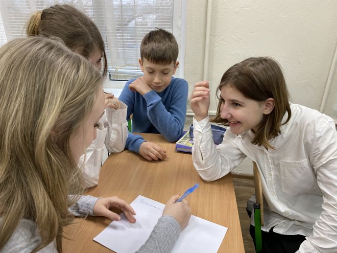  denne Fire barn sitter rundt et bord og samarbeider om en oppgave med papir og penn.
