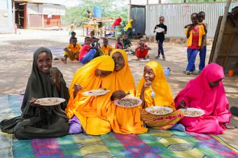 A group of young girls stand outdoors, wearing colourful headscarves and clothing.