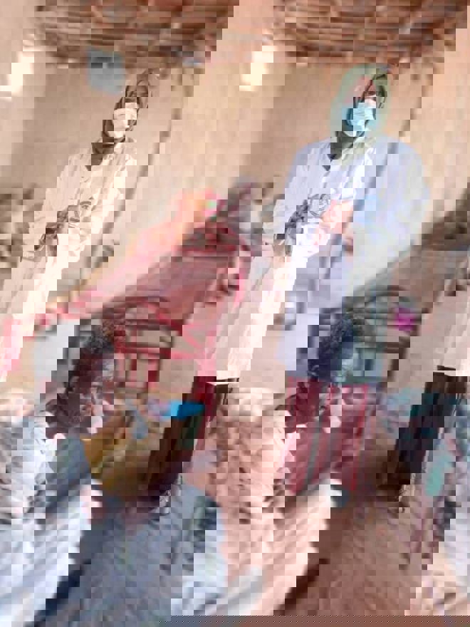 En voksen kvinne i hvit frakk og hijab står inne i et rom på et sykehus, og en eldre mann sitter på en seng foran henne.