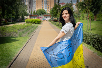 En ung kvinne står på en gangvei i en park og holder et ukrainsk flagg med håndskrevet tekst.