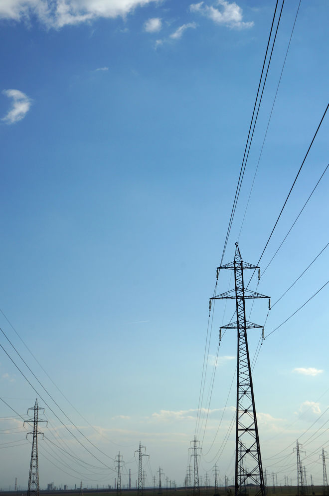 Høye kraftmaster med strømledninger strekker seg over et åpent landskap under blå himmel.
