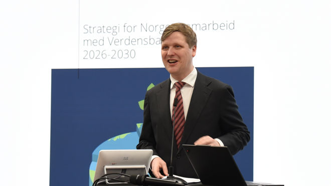 En ung mann i dress holder en presentasjon foran en skjerm med teksten "Strategi for Norges samarbeid med Verdensbanken 2026–2030. 