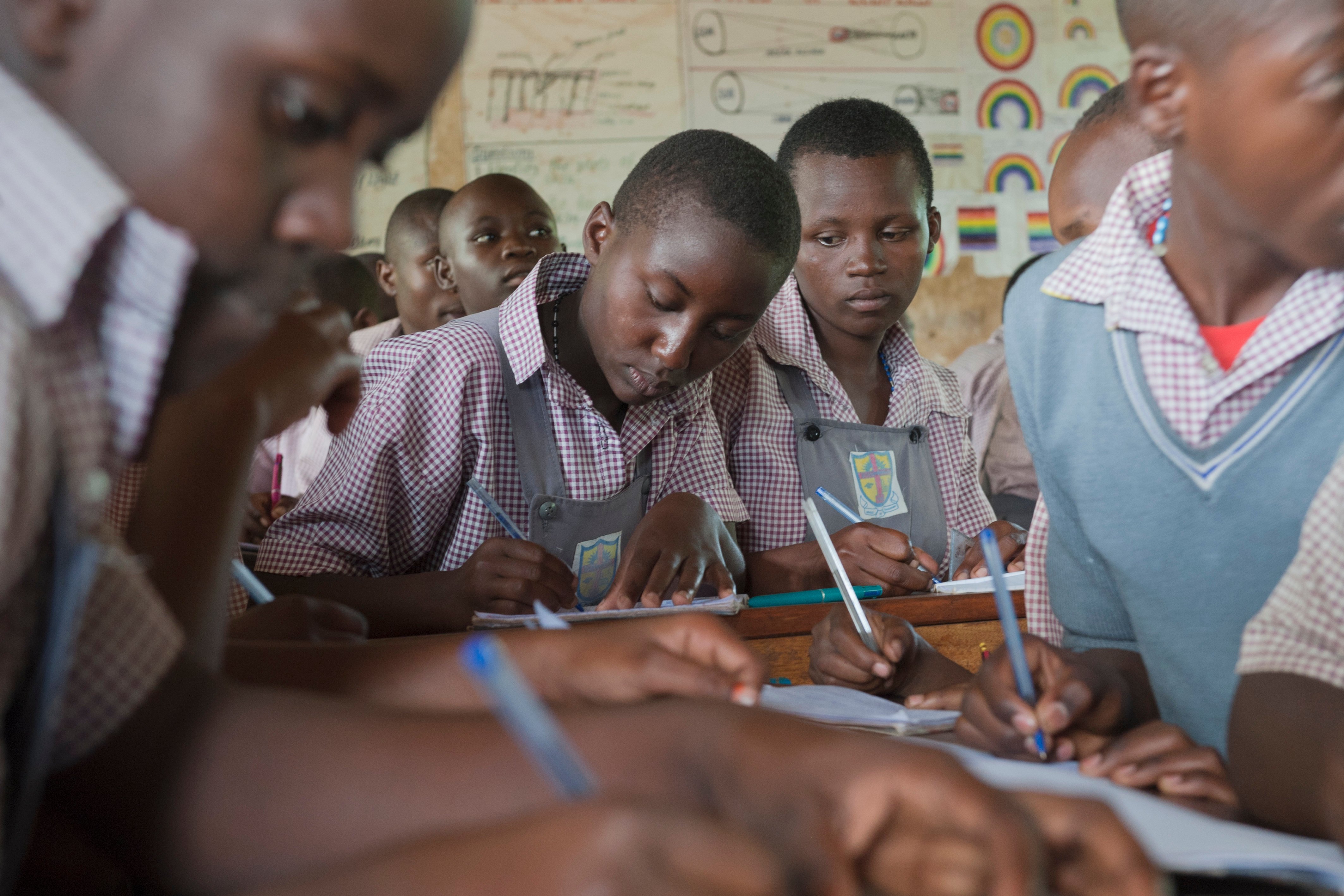 Elevar i skuleuniform sit og skriv ved pultar i eit klasserom.