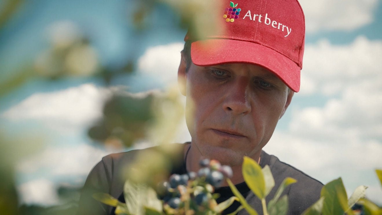 Close-up of a man wearing a red cap standing outside among the trees.