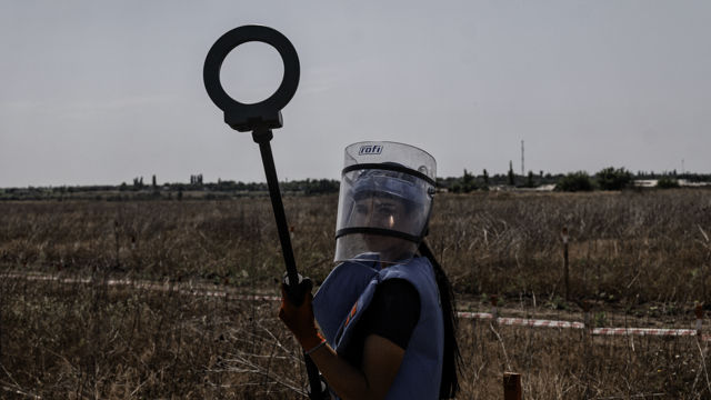 Mann med mineverktøy i hendene står alene ute i tørt landskap.