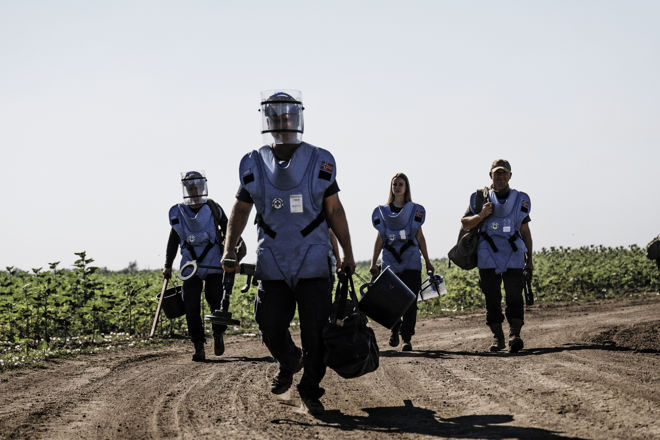 Fire mennesker i blå vester går på en grusvei ute.