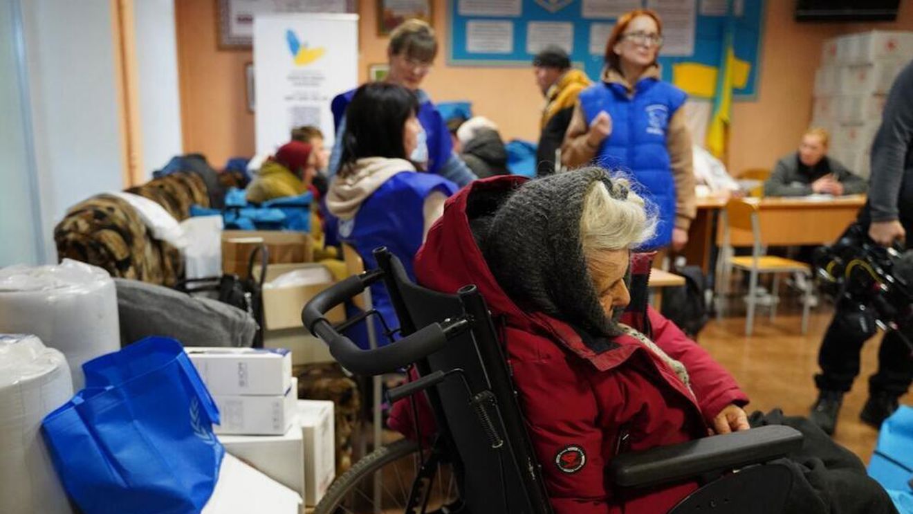 Eldre kvinner sitter på mottakssenter i rullestol.