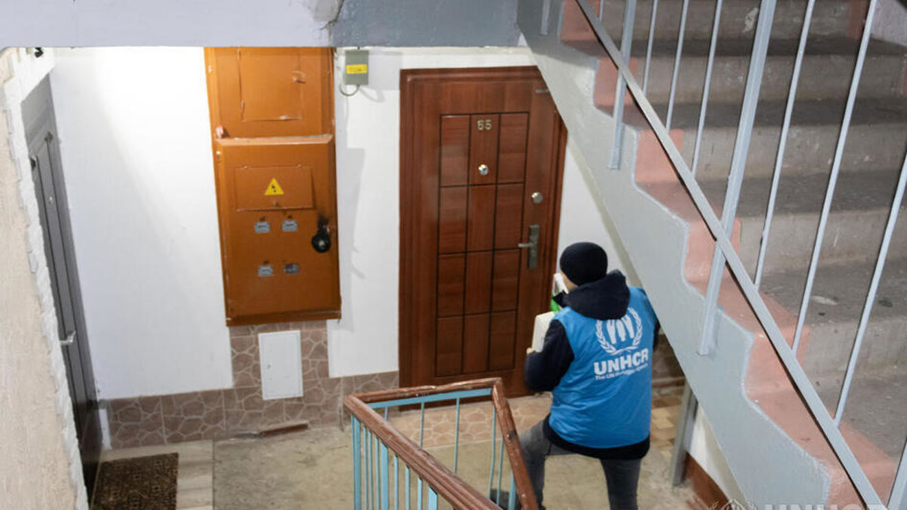 A man wearing a UNHCR vest is walking up the stairs inside a building