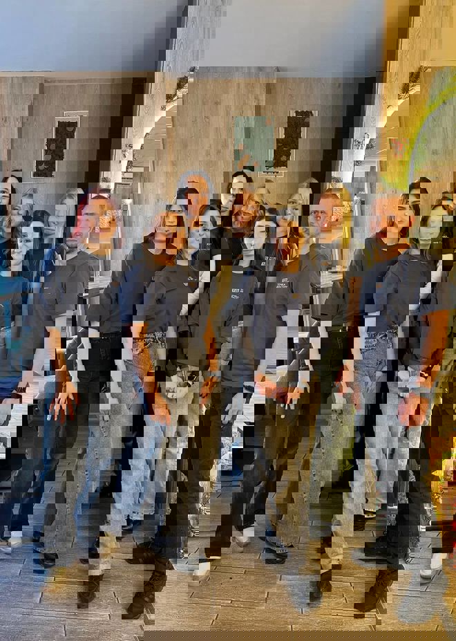 A group of young adults stand together indoors, all wearing matching dark t-shirts and jeans.