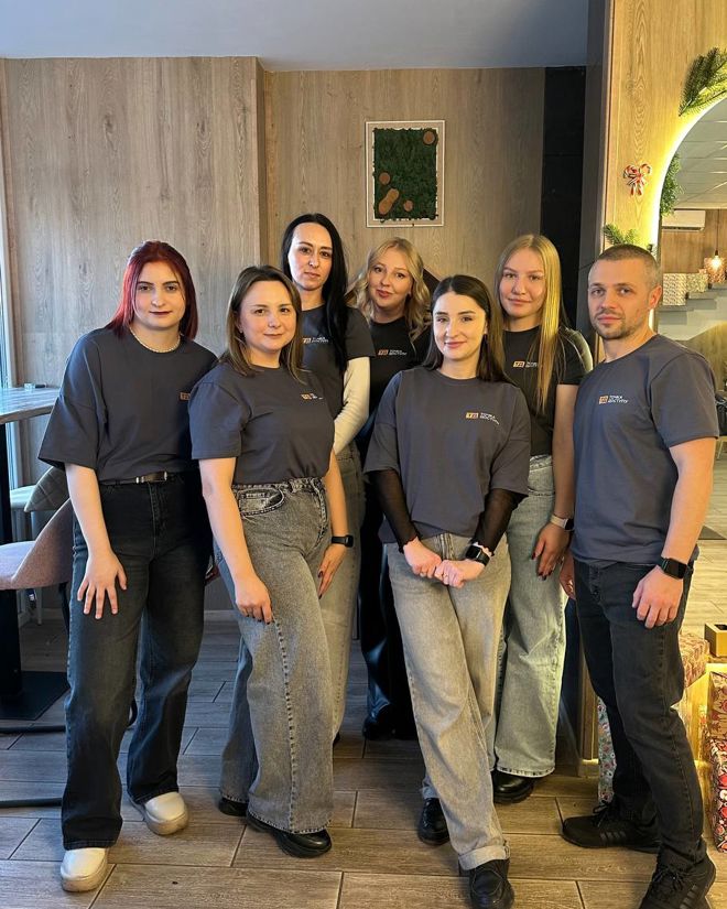 A group of young adults stand together indoors, all wearing matching dark t-shirts and jeans.