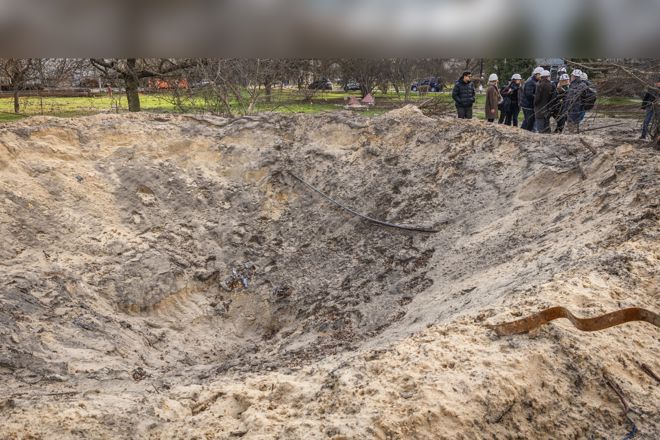 A large crater in the ground with a group of people standing at the edge observing it.