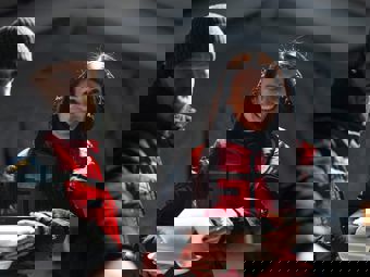 Two adults wearing red jackets are handing out food in takeaway containers indoors.