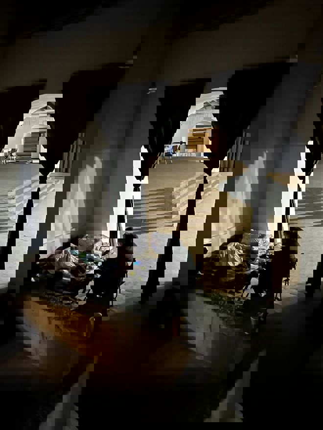 A person sitting with a phone while two other people are sleeping inside of a church building. 