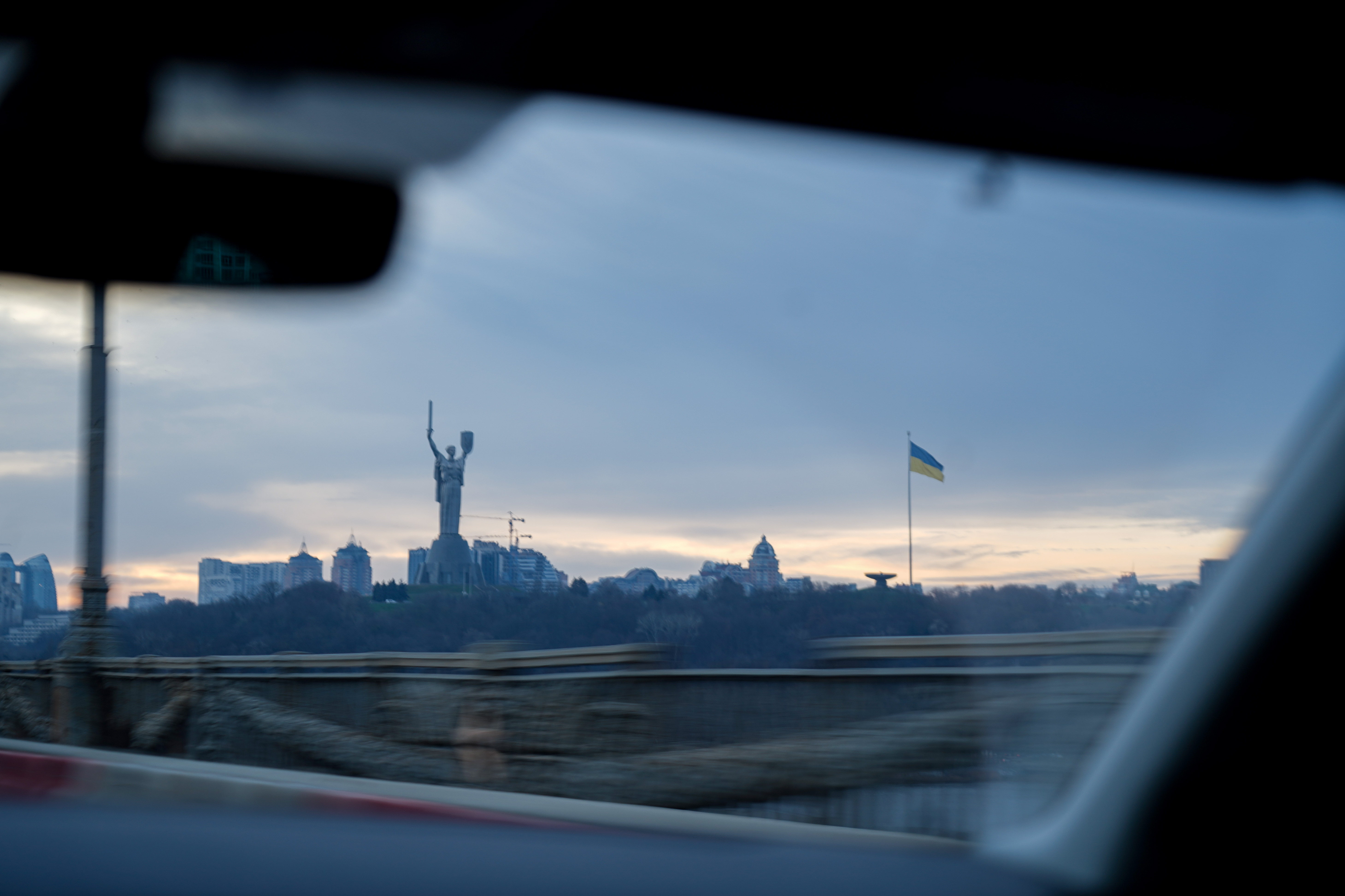 Utsikt mot Moderlandet-statue og ukrainsk flagg i Kyiv, sett gjennom frontruten på en bil.