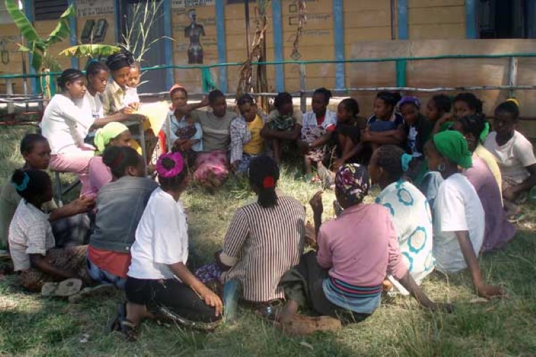 En grupper jenter sitter i ring på gresset. Etiopia.