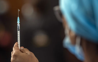 En helsearbeider med blått hodeplagg holder opp en sprøyte klar for bruk.