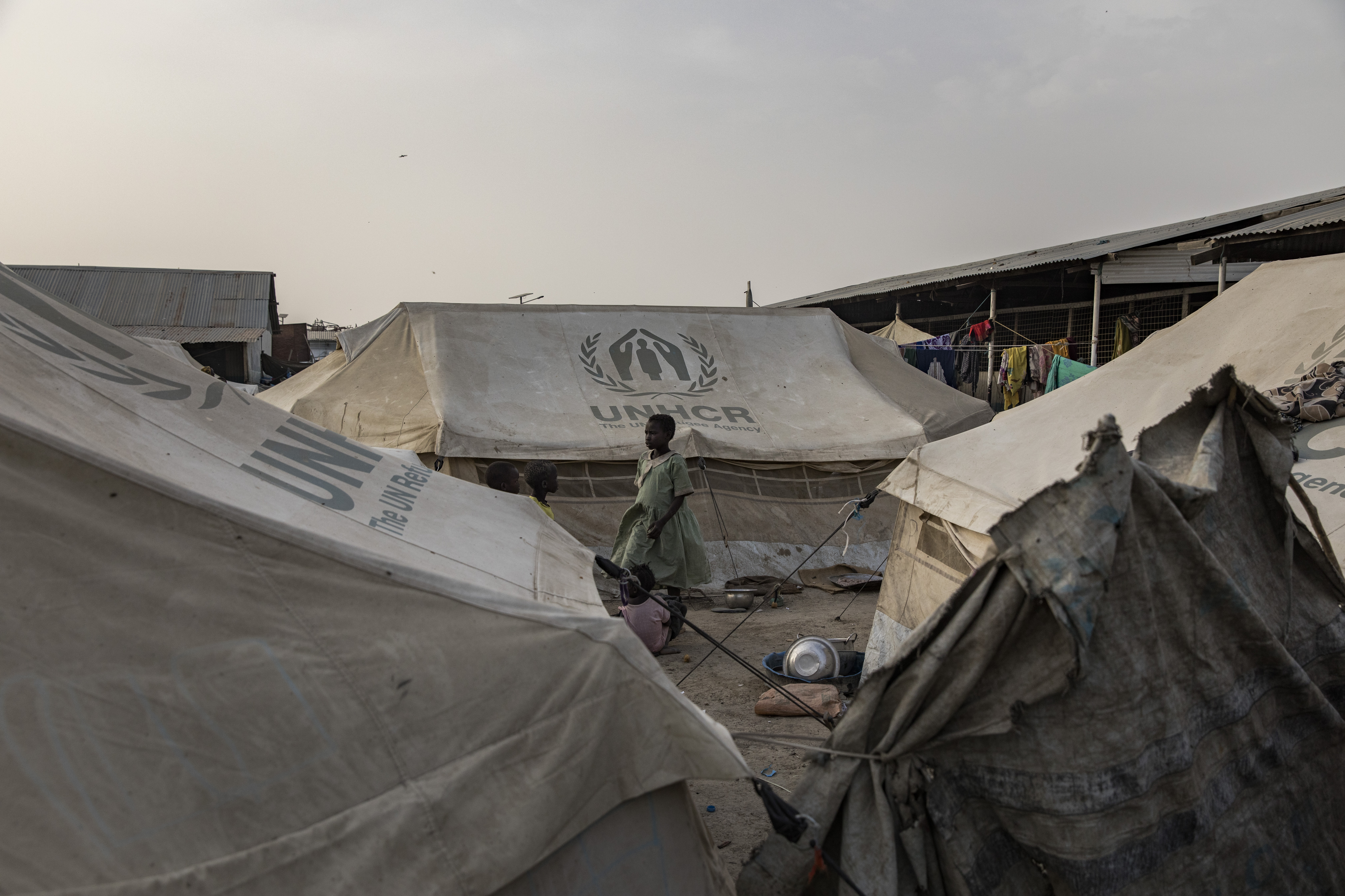 En kvinne og et barn står mellom UNHCR-telt i en flyktningleir, med klær som henger til tørk i bakgrunnen.